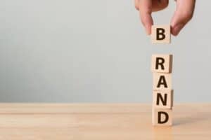 Fingers stacking blocks on table that spell "brand."